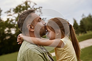 Young loving father kissing his cute little daughter in forehead while spending time together outdoors on a summer day