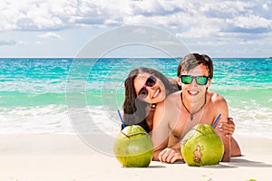 Young loving happy couple have fun on tropical beach, with coconuts. Summer vacation concept.