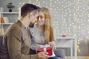 Young loving happy couple woman and man sitting together on sofa and opening holiday present box