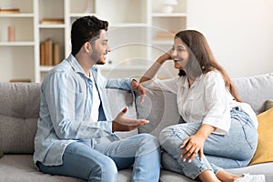 Young loving indian couple talking and flirting enjoying conversation at home, spending time together sitting on sofa photo