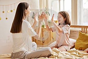 Young loving mom and cute little daughter wearing pajamas having fun at home, enjoying time together in bedroom