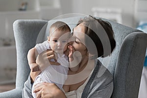 Young loving mother kisses baby cheek, closeup