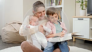 Young loving mother sitting with her sons in living room and reading story book. Parenting, children happiness and