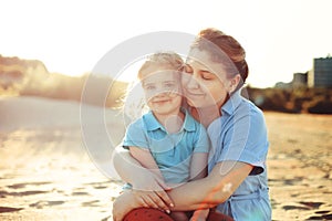 Young loving mother with smiling daughter hugging her little daughter on sunny beach