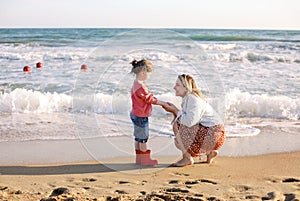 Young loving mother with smiling daughter running on sunny beach