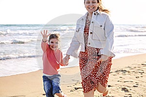 Young loving mother with smiling daughter running on sunny beach