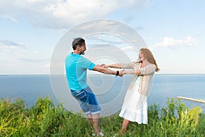 Young loving smiling couple in grass on lake and sky background. Shot of attractive young red hair woman dancing with boyfriend