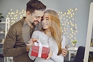 Young loving smiling couple standing, hugging and opening present box during Valentines day