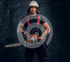 Young lumberjack wearing protective clothes posing with a chainsaw in a dark studio