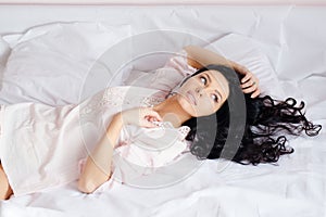 Young magic beautiful charming woman in white shirt lying on the bed & looking in window on white background closeup portrait