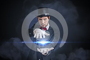 Young magician man is showing bright ball that levitates. Black background