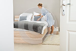 Young maid arranging pillow on bed photo