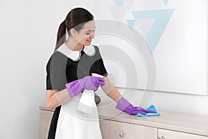 Young maid cleaning furniture with rag