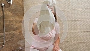 Young maid cleaning and wiping stains on glass door at shower in hotel room.