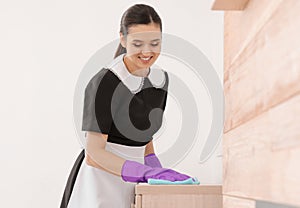 Young maid dusting furniture with rag