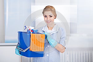 Young maid holding cleaning supplies