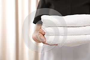 Young maid holding stack of fresh towels in hotel room