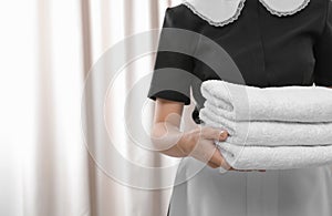 Young maid holding stack of fresh towels in hotel room, closeup