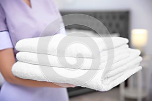 Young maid holding stack of towels in hotel room