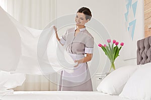 Young maid making bed in hotel