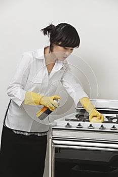 Young maidservant cleaning stove against gray background photo