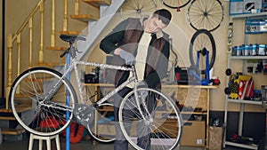 Young maintenance man is assembling bicycle placing stearing wheel and fixing it while listening to music with earphones