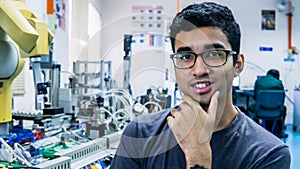 A young Malay engineering student with spectacles working in the lab and thinking by holding chin