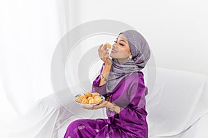 Muslim Malay girl celebrates end of Ramadan, in purple dress with hijab, and holding food
