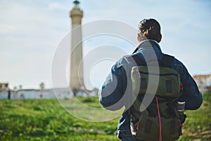 Young male adventurer tourist standing back to camera, looking at a lighthouse on the nature. Travel, active lifestyle