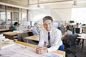 Young male architect in busy office smiling to camera