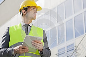 Young male architect with digital tablet looking away outside building