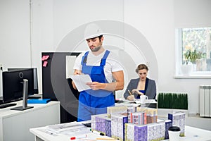 Young male architect in a white hard hat and overalls working in