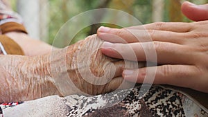 Young male arms comforting an elderly pair of old woman hands outdoor. Grandson and grandmother spending time together