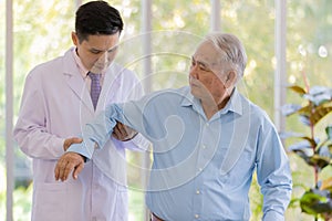 A young male asian black hair doctor wearing white lab coat holding the patient arm and checking his elbow when the senior white