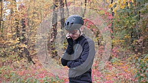 Young male athlete in cycling apparel, helmet and glasses dialing phone number and calling on smartphone before workout in fall fo