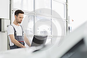 Young male automobile mechanic using computer in repair shop