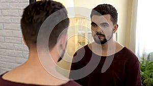 Young male bachelor looking in mirror in morning, appearance insecurities photo