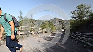 Young male backpacker going uphill along ground road in mountains on sunny day