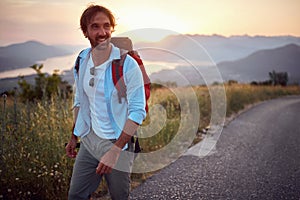 Young male backpacker on road alone, walking on road in nature. Travel, camping, recreation, nature concept