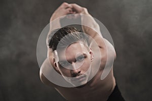 A young male ballet dancer with black leggings and a naked torso performs dance moves against a gray grunge background