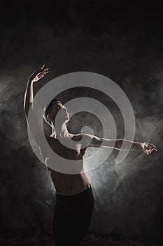 A young male ballet dancer with black leggings and a naked torso performs dance moves against a gray grunge background