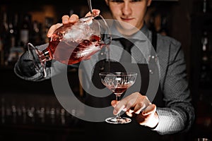 Young male barman pouring a fresh alcoholic cocktail into the cocktail glass