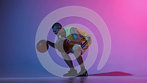 Young male basketball player dribbling two basketball balls at once over gradient blue pink neon background. Sport