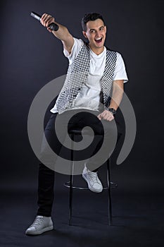 Young male black-haired pop singer posing singing to microphone