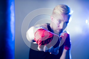 A young male boxer is doing sports in the gym. boxer, puts on boxing gloves on a dark background. the man strikes. red