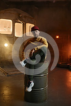 Young male breakdancer sitting on steel barrel tank