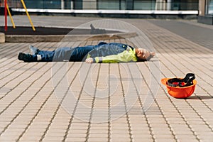 A young male builder died lies on the pavement in special construction clothing. Construction site accident