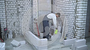 Young male builder moisturing block with water sprayer before laying it