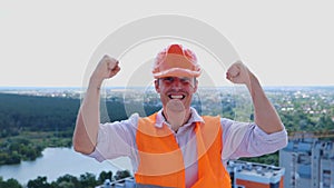 Young male builder wearing construction uniform and safety helmet celebrating crazy on the roof. Business, building