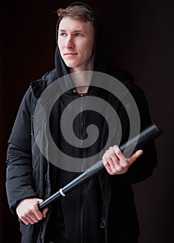 A young male bully with a baseball bat in his hands, looks away.